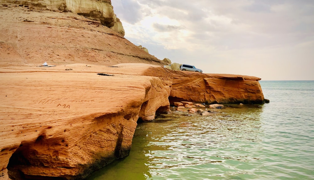 white and black van on brown rock formation beside body of water during daytime