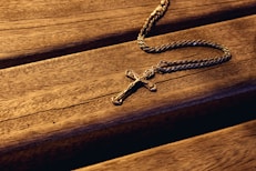 silver cross pendant on brown wooden surface