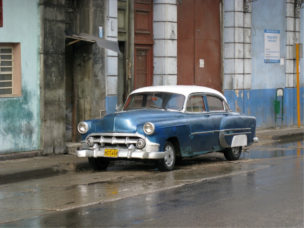 blue classic car parked beside brown concrete building during daytime