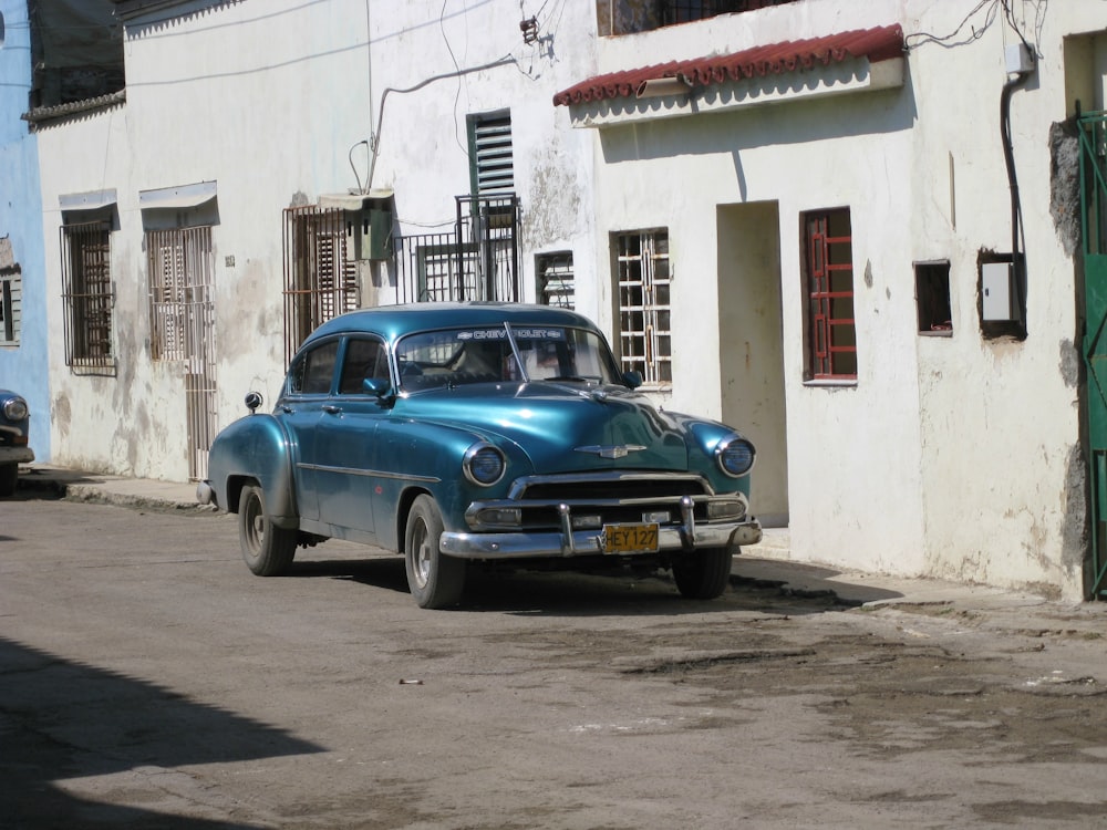 blue sedan parked beside white concrete building during daytime