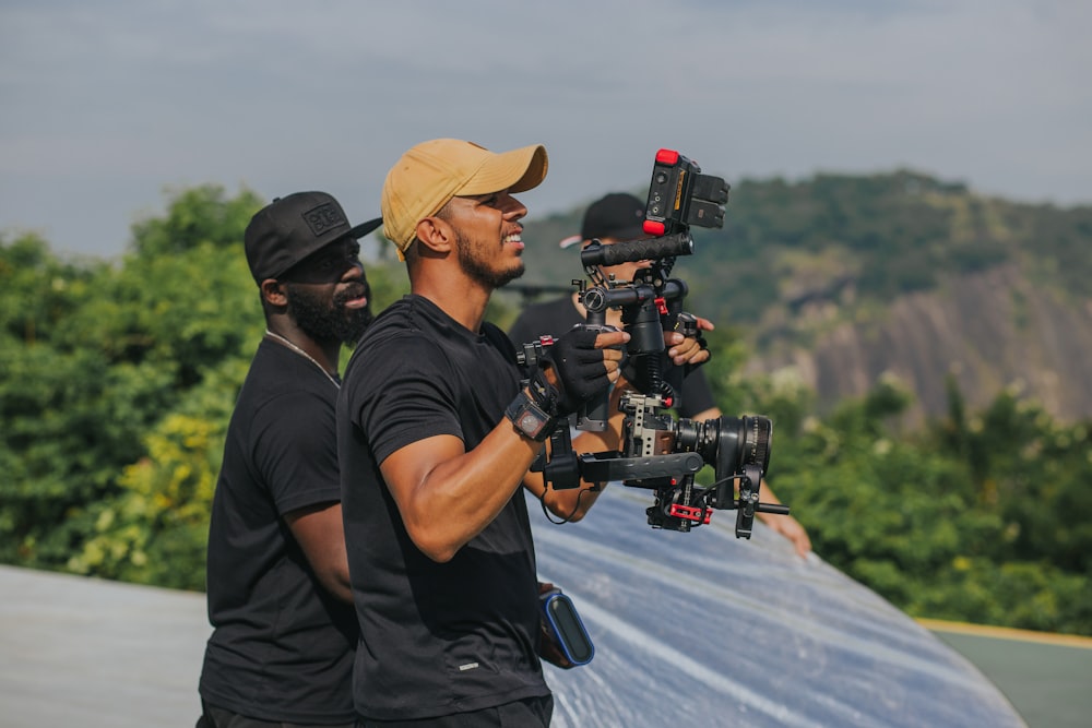 man in black t-shirt and brown hat holding black dslr camera