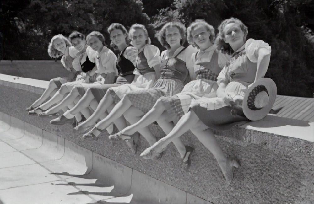 grayscale photo of group of women sitting on concrete bench