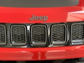 A close-up view of the front grille of a red Jeep vehicle, featuring a black hexagonal pattern and the Jeep logo prominently displayed above it.