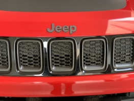 A close-up view of the front grille of a red Jeep vehicle, featuring a black hexagonal pattern and the Jeep logo prominently displayed above it.