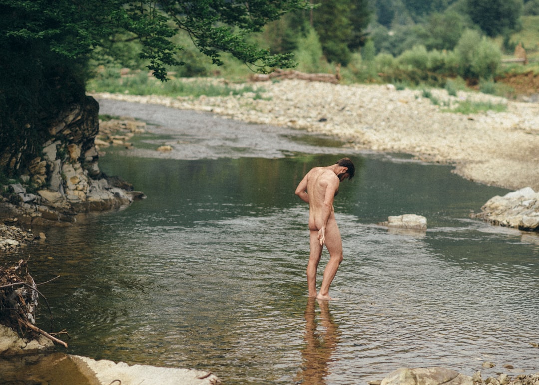 topless man standing on river during daytime