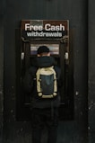 man in blue and yellow jacket and black backpack standing in front of brown wooden door