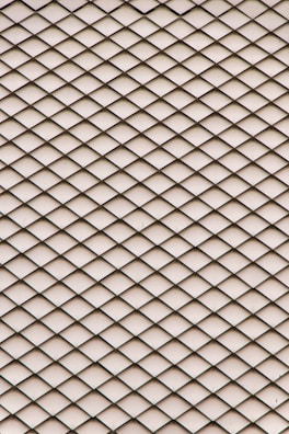 A geometric pattern consisting of overlapping diamond-shaped tiles creates a textured and rhythmic effect. The tiles are uniformly arranged, forming a seamless, repetitive design across the surface.