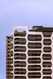 A modern, high-rise building featuring a unique honeycomb-like facade with reflective glass panels. The structure has a combination of straight and curved lines, creating a dynamic architectural appearance.