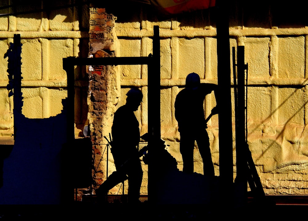 silhouette of 2 men standing on a ladder