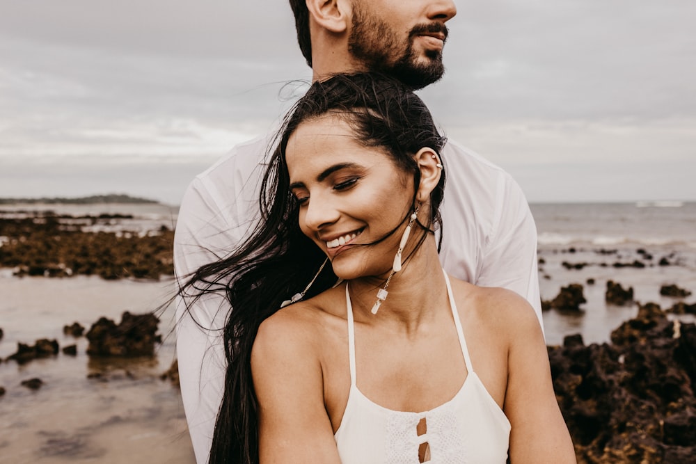 man in white tank top kissing woman in white spaghetti strap top on beach during daytime