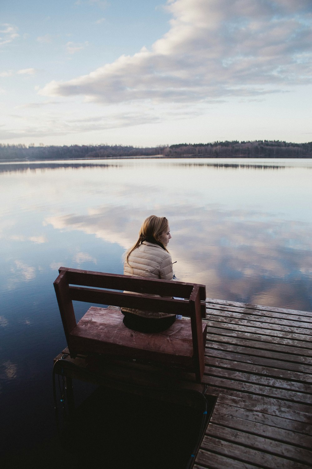 woman in gray hoodie sitting on brown wooden dock during daytime