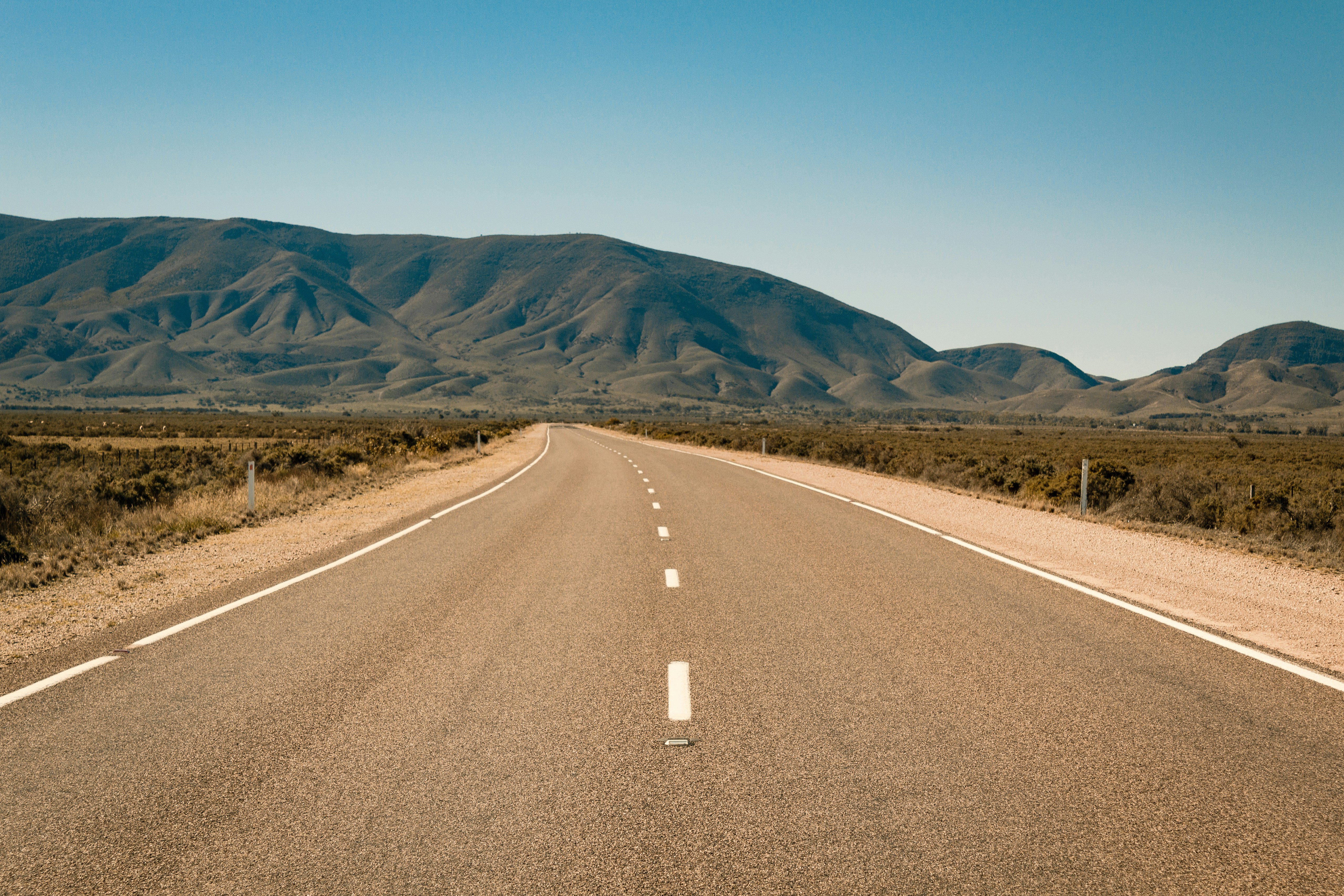 gray concrete road near brown mountain under blue sky during daytime