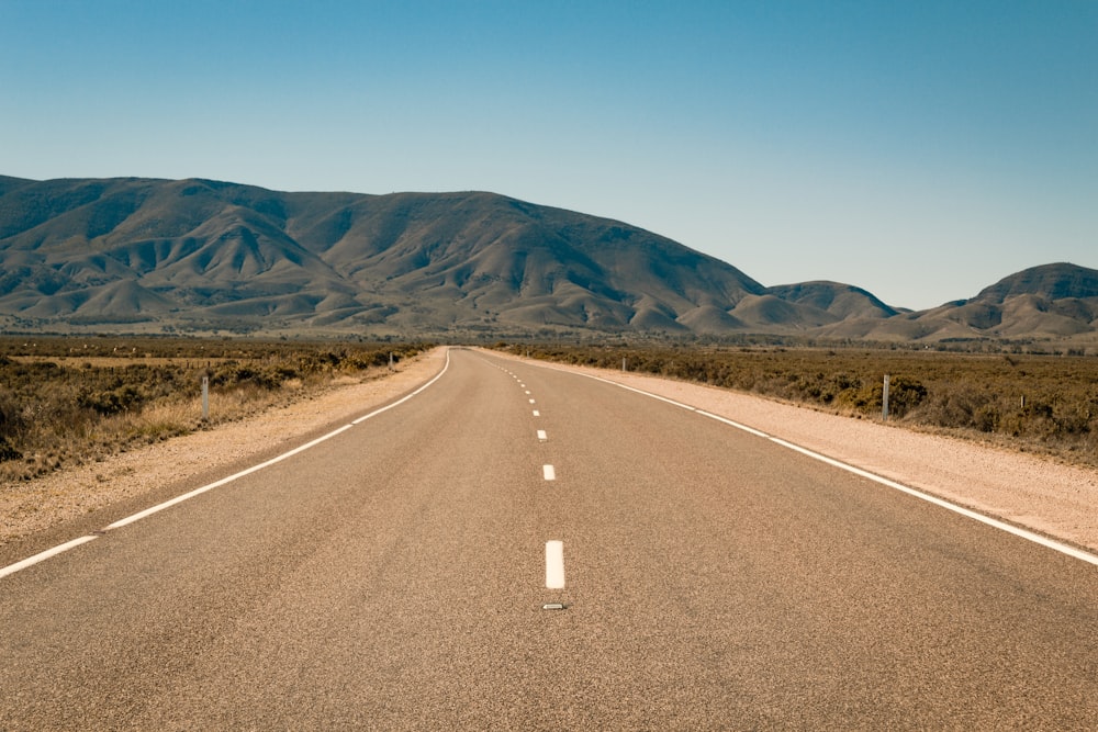 gray concrete road near brown mountain under blue sky during daytime