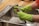 A person wearing bright green rubber gloves is washing a kitchen tap over a stainless steel sink. The setting appears to be a domestic kitchen with a wooden countertop.