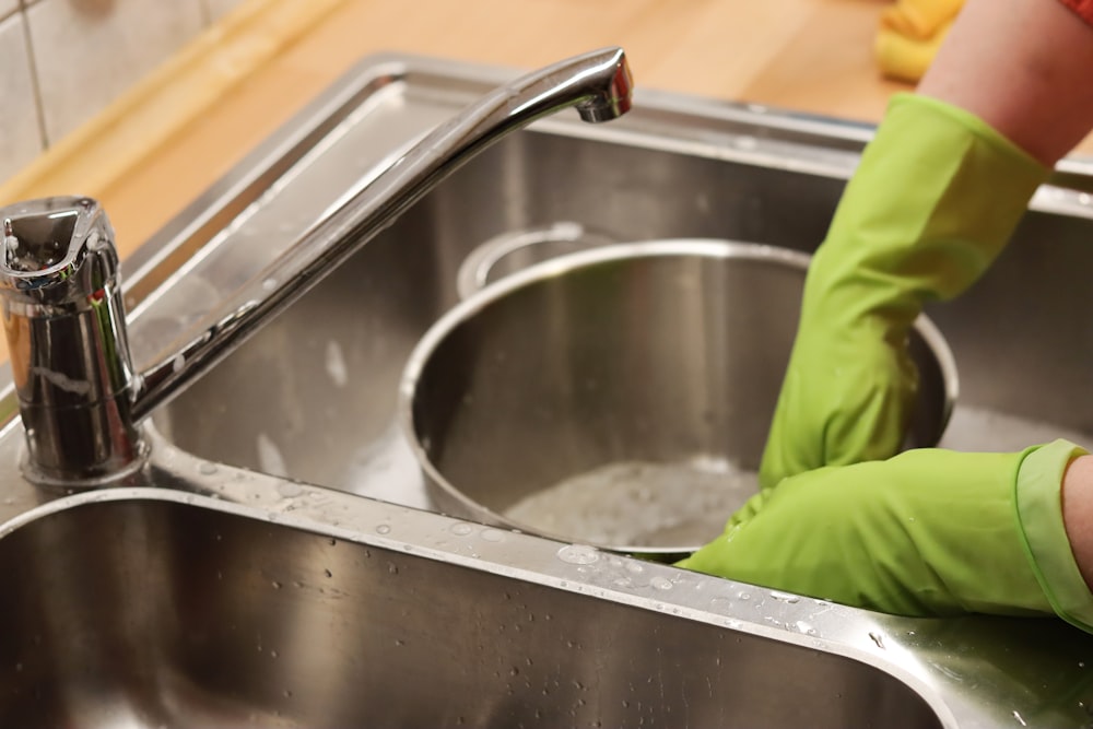 person in green shirt washing stainless steel sink