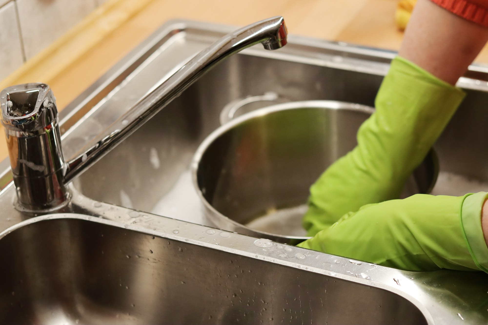 Wasserhahn und Abwasch mit grünen Handschuhen