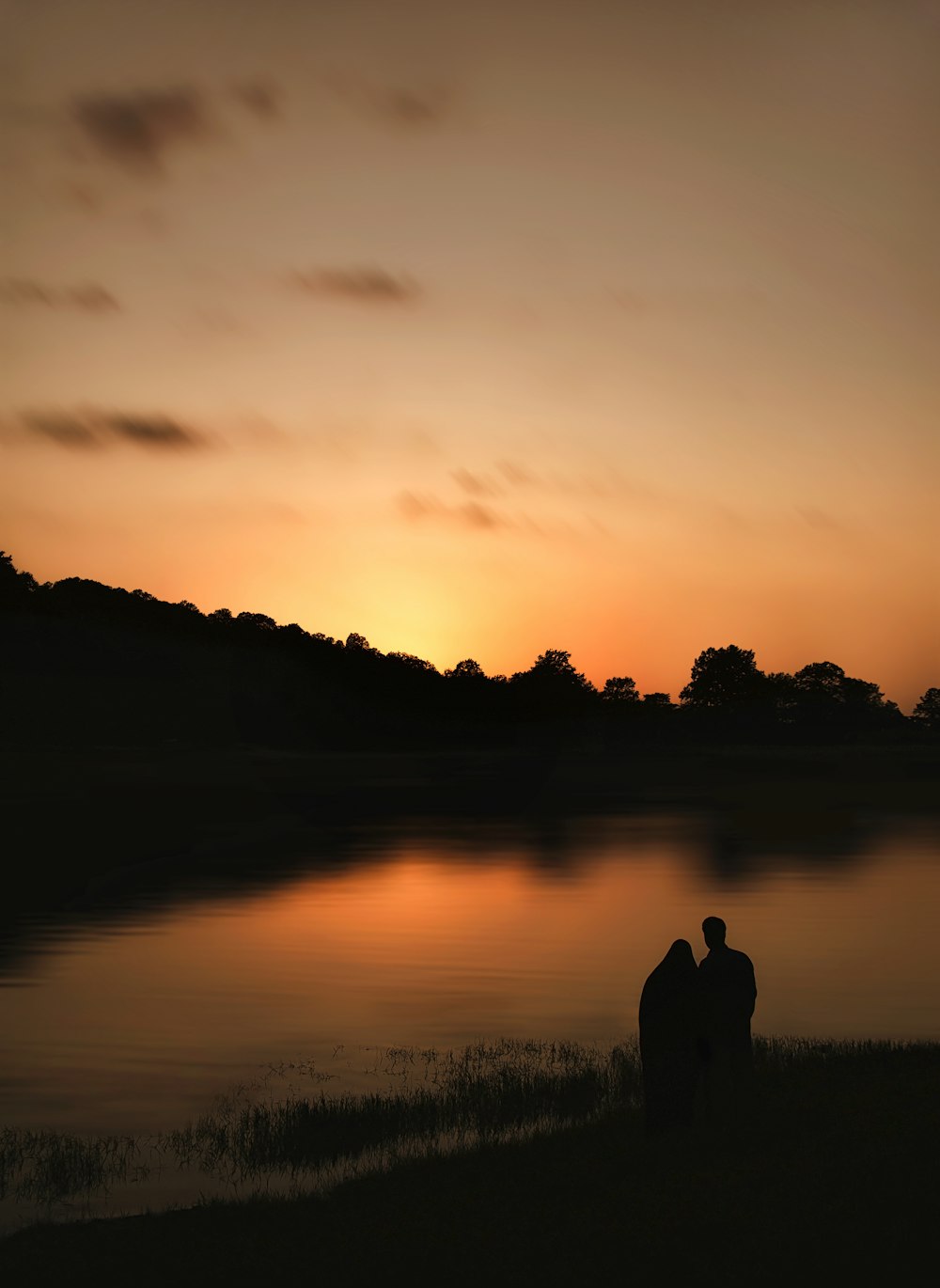 silhouette of man and woman standing near lake during sunset