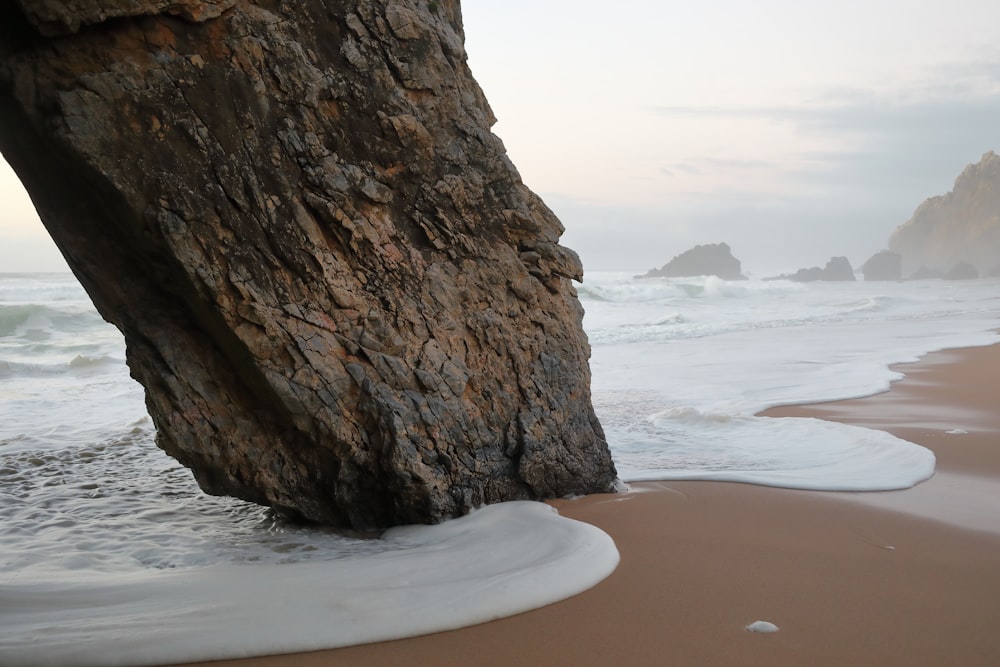 formação rochosa marrom na praia durante o dia