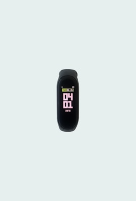 A sleek, black fitness tracker displays the date and time on its screen, with numbers in pink and information in light green and white. It is centered on a plain, light gray background.