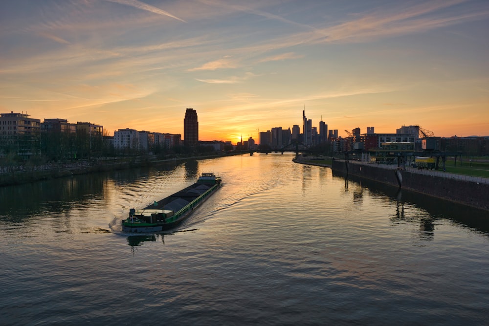 green boat on water near city buildings during sunset