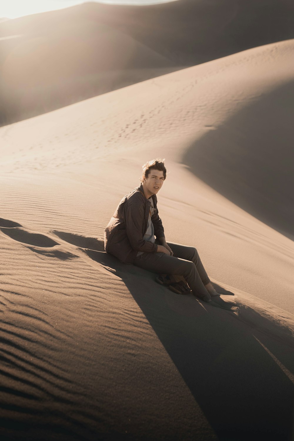 man in brown jacket sitting on sand