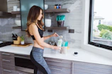 woman in black tank top and blue denim jeans holding clear plastic bottle