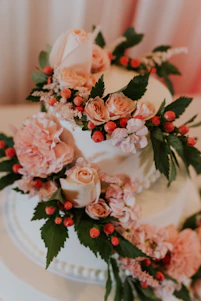 Close-up of a delicate blush pink and cream frosted cake adorned with edible gold leaf and fresh flowers.