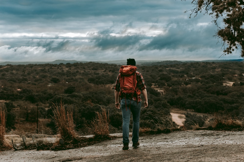 woman in brown jacket and blue denim jeans standing on rock formation under white clouds during