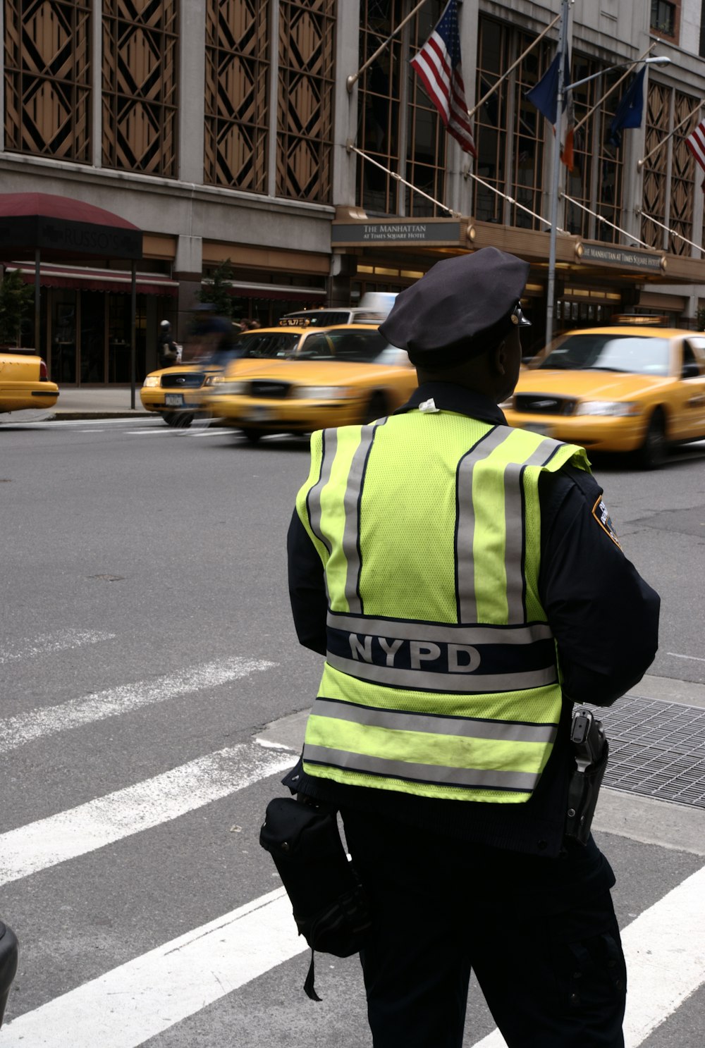 man in green and black jacket wearing black hat standing on sidewalk during daytime