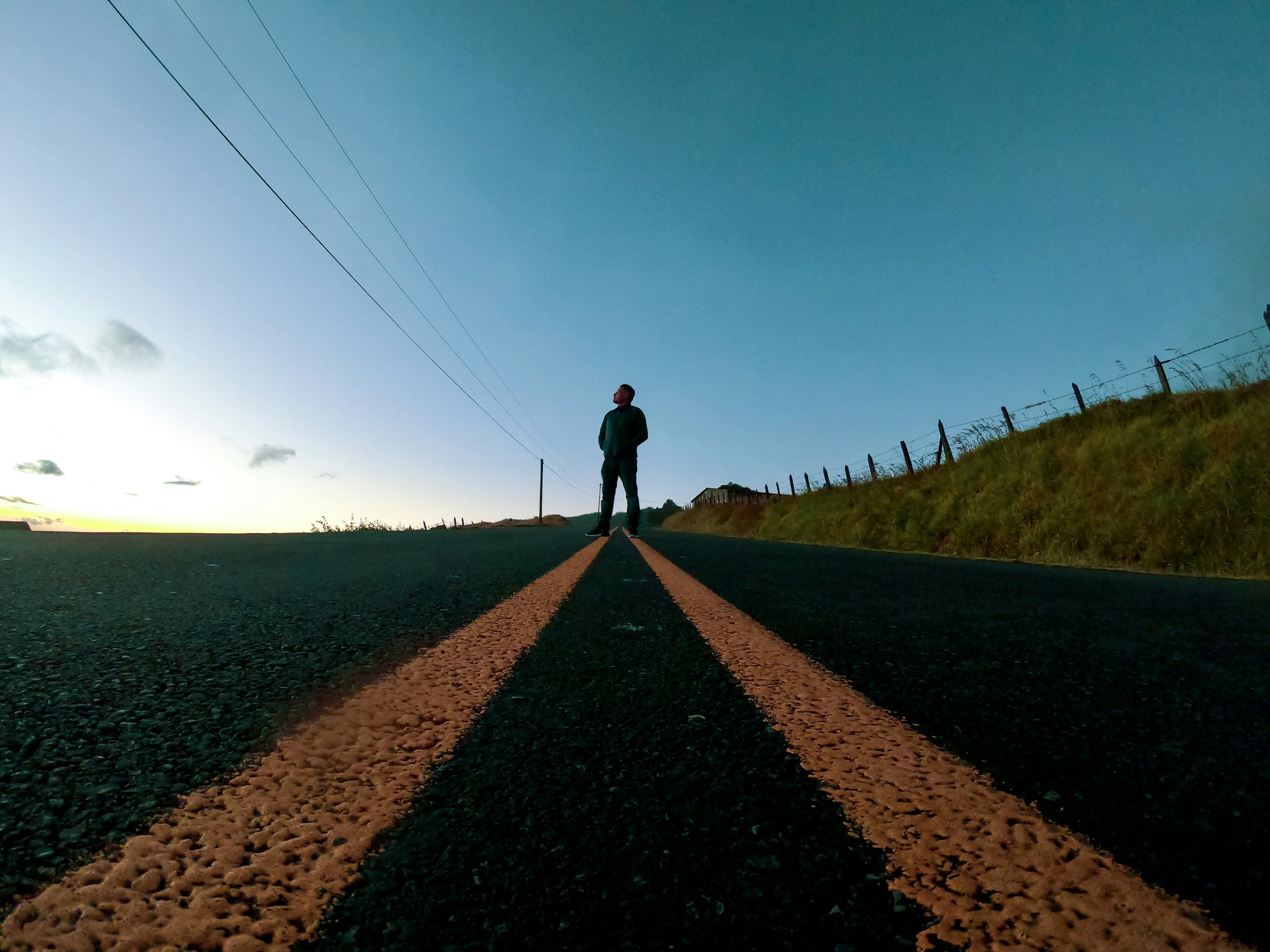 Man standing alone on empty road at dusk looking toward horizon