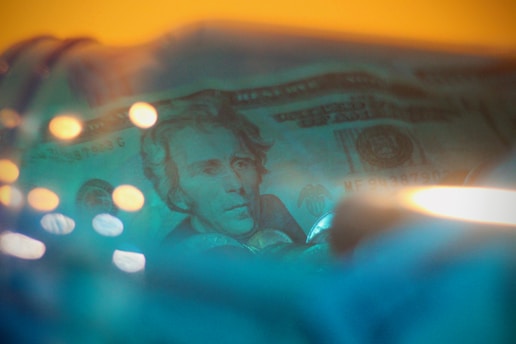 A close-up of hands exchanging cash with a blue gradient background featuring subtle bill details.