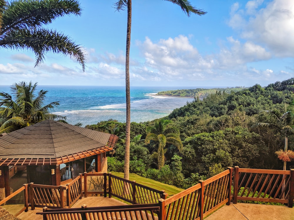 A fenced wooden house atop a green mountain with the ocean at the bottom.