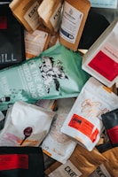 A variety of coffee bags scattered, showcasing different brands and blends. The packaging features colorful designs with text and graphics, including names and descriptions of each coffee blend.