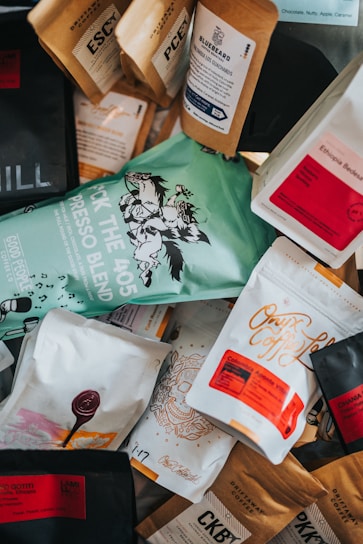 A variety of coffee bags scattered, showcasing different brands and blends. The packaging features colorful designs with text and graphics, including names and descriptions of each coffee blend.