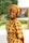 A woman is smiling while wearing a traditional African outfit. The fabric has a yellow pattern with black details. She is standing outdoors with green foliage in the background, giving a relaxed and natural setting.