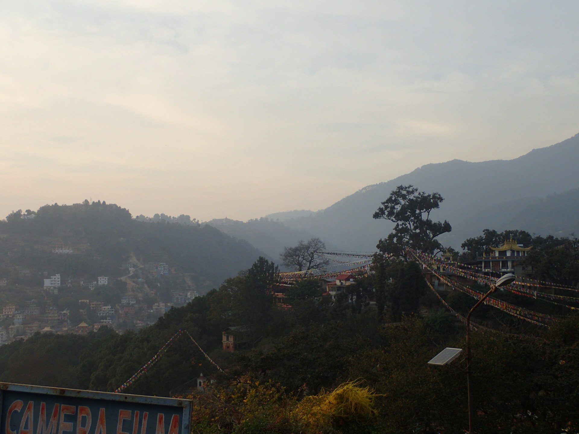 A serene mountain village at sunset, with prayer flags fluttering gently and warm lights glowing from stone lodges.