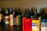 Several bottles of colored ink are arranged on a dark surface, each with a pointed cap. The inks are in various colors including red, yellow, orange, green, and more with labels on each bottle. The background is a neutral shade, slightly out of focus, allowing the vibrant colors of the bottles to stand out.