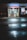 The front entrance of a family drug store named 'Alpha Pharmacy' at night, illuminated by bright, artificial lighting. The pavement in front of the store is wet, reflecting the store's lights. There is a sign above the entrance displaying 'Family Drug' prominently.
