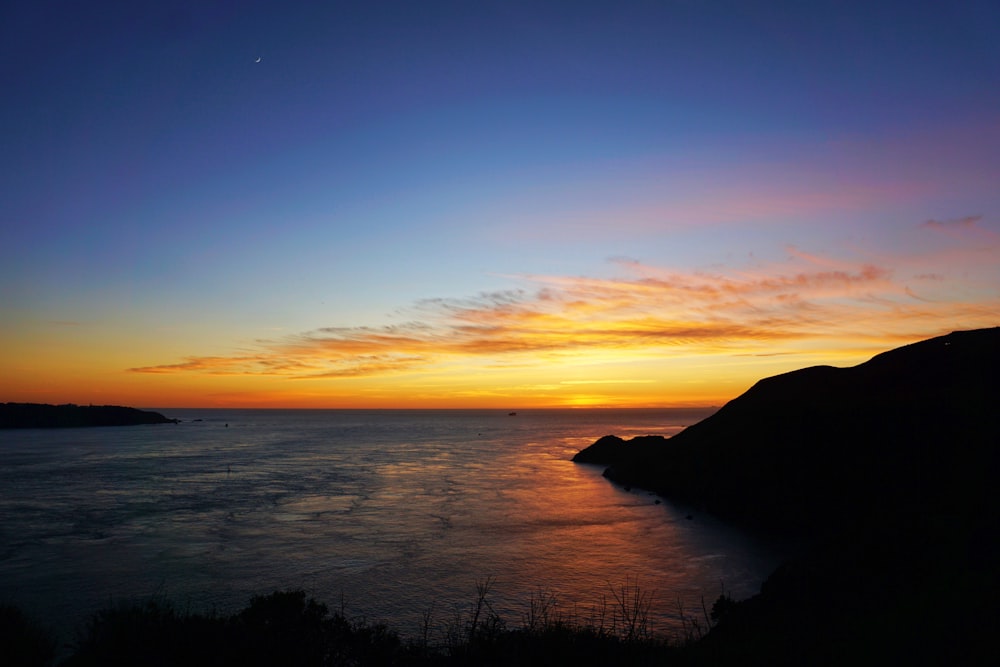 silhouette of mountain near body of water during sunset