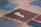 Several colorful, square tiles with rough, textured surfaces arranged on the ground. One tile prominently features a stylized white footprint with a spiral design on a dark brown background. The surrounding tiles are shades of blue and red.