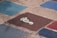 Several colorful, square tiles with rough, textured surfaces arranged on the ground. One tile prominently features a stylized white footprint with a spiral design on a dark brown background. The surrounding tiles are shades of blue and red.