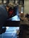 A person is engaged in welding, wearing a protective helmet with flame designs. Bright sparks are flying around, and a blue light emits from the welding area. The setting appears to be an industrial workshop with metallic surfaces and various equipment in the background.