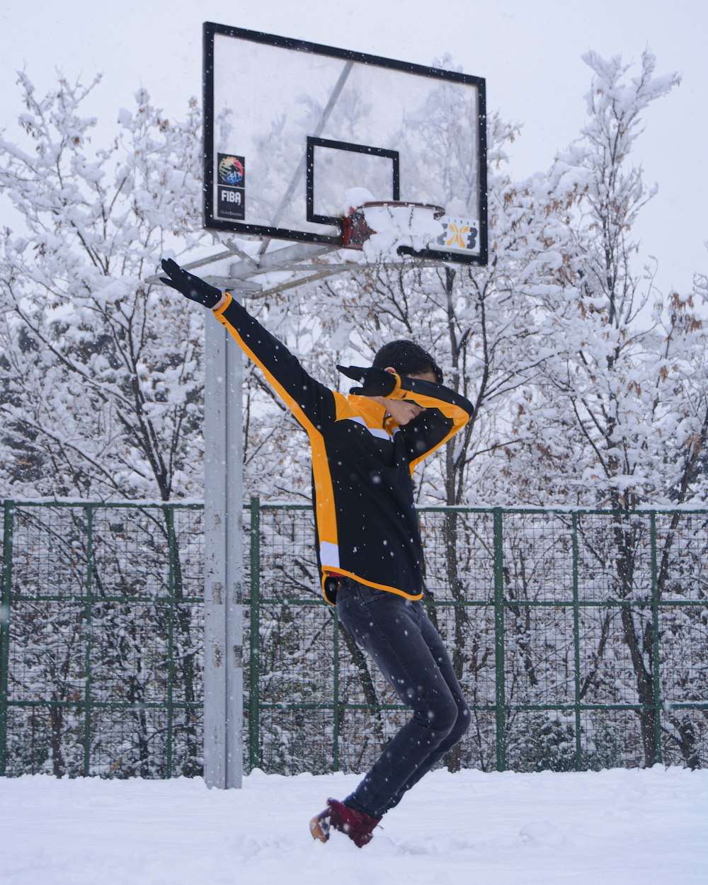 Mann in schwarz-gelber Jacke und schwarzer Hose, der tagsüber auf einem Basketballkorb steht