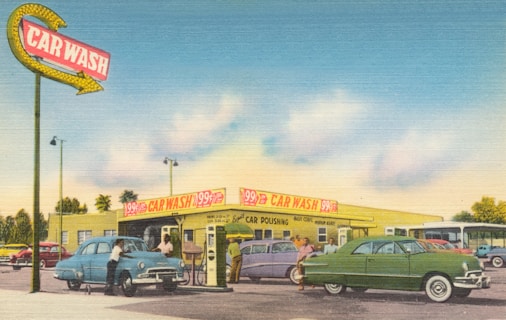 A vintage car wash scene featuring classic cars and a large, retro sign that reads 'Car Wash'. There are several cars parked, including a blue and a green one, with people around them, seemingly getting their vehicles cleaned. The building in the background displays signs advertising car wash services for 99 cents. The setting includes clear blue skies with a few clouds, giving off a sunny day vibe.