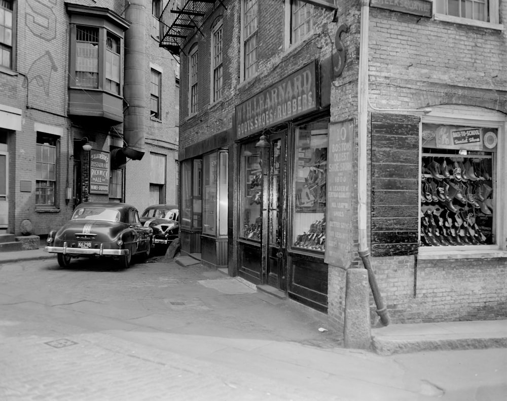 grayscale photo of cars parked beside building