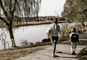 A mother and daughter walking hand in hand along a scenic lakeside trail.