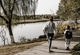 A mother and daughter walking hand in hand along a scenic lakeside trail.