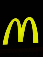 A bright yellow, large and bold 'M' shape against a stark black background, symbolizing a well-known fast-food brand.