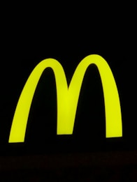 A bright yellow, large and bold 'M' shape against a stark black background, symbolizing a well-known fast-food brand.