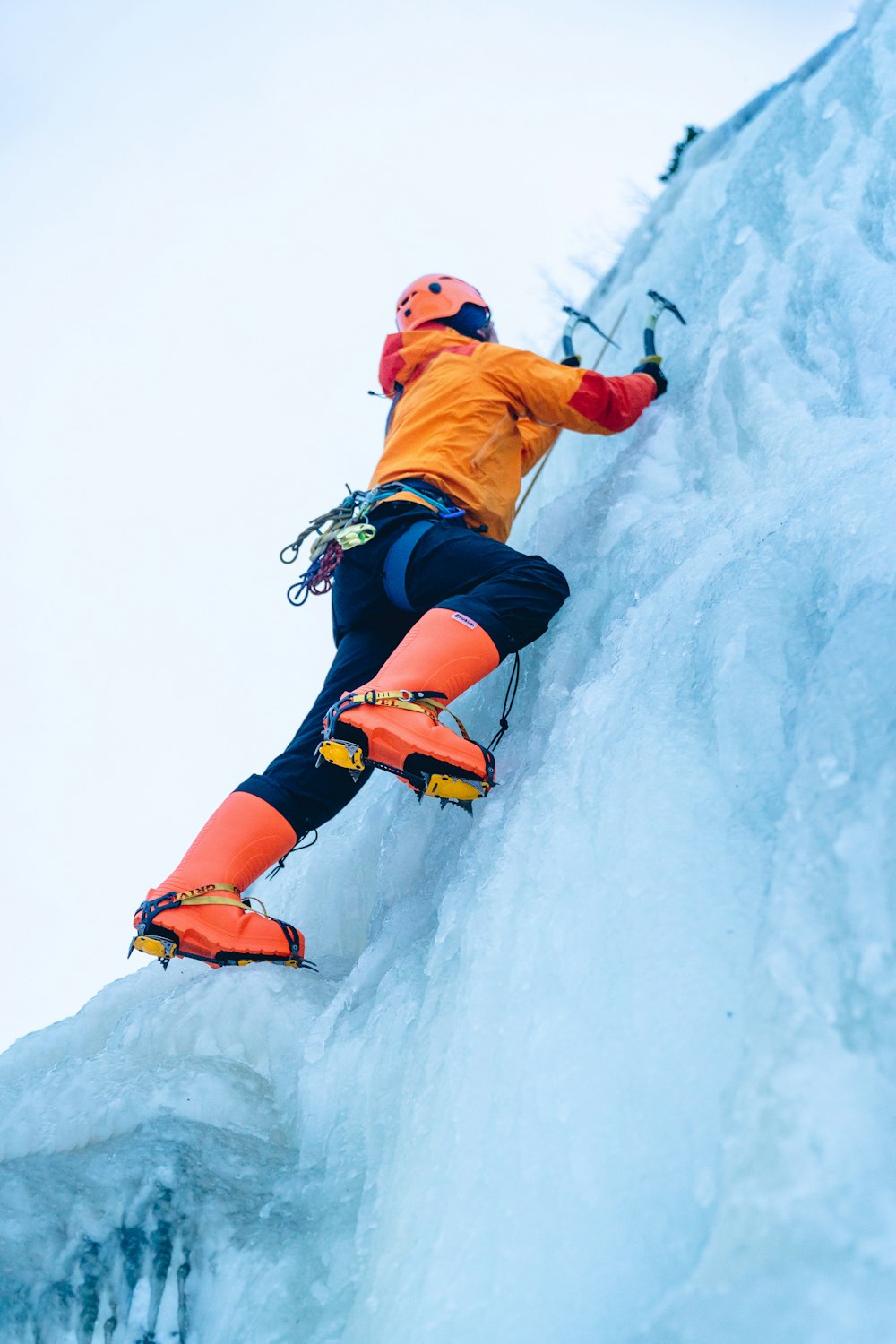 Mann in orangefarbener Jacke und blauer Jeans mit schwarzem Helm auf schneebedecktem Boden